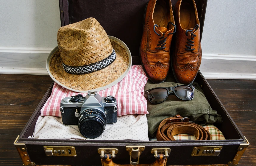 vintage-hipster-clothes-shoes-hat-smartphone-accessories-packed-in-suitcase-on-wooden-floor.