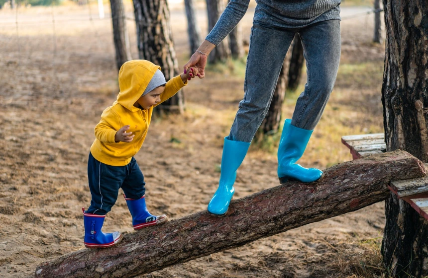 baby walks on a wood holding parent's hand